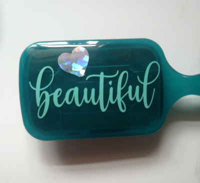 Teal hairbrush with 'beautiful' text and heart design on a white background